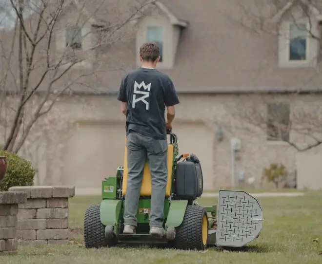 A Royal Acres crew member on a stand-on mower in front of a house