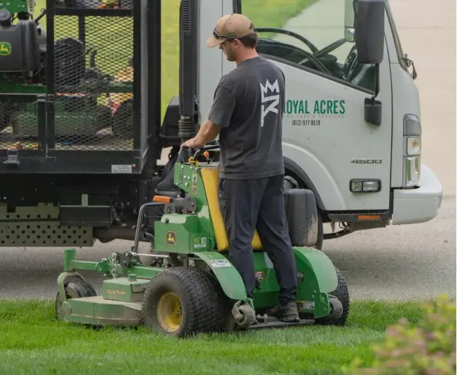 A Royal Acres crew member on a stand-on mower beside the company truck