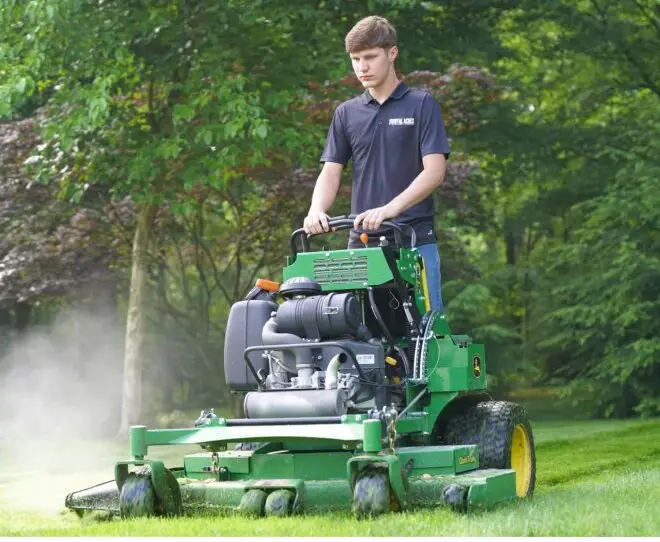 A Royal Acres crew member mowing on a stand-on mower