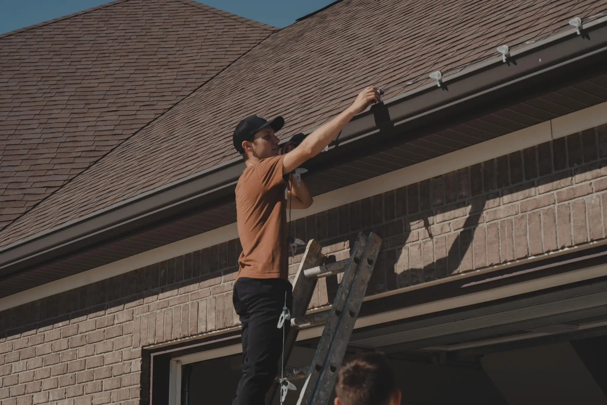 A crew member on a ladder fixing light clips along a gutter