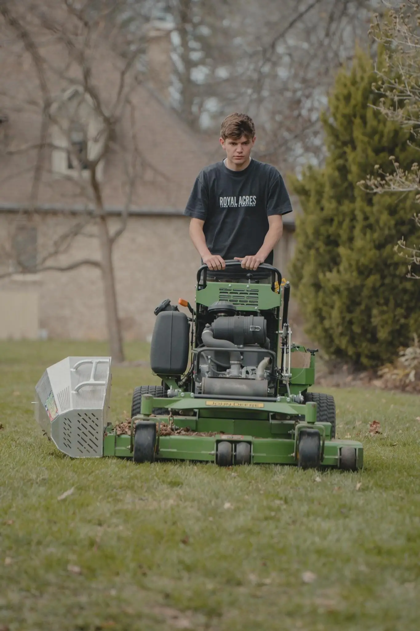 A crew member mowing a front lawn on a stand-on mower in early spring