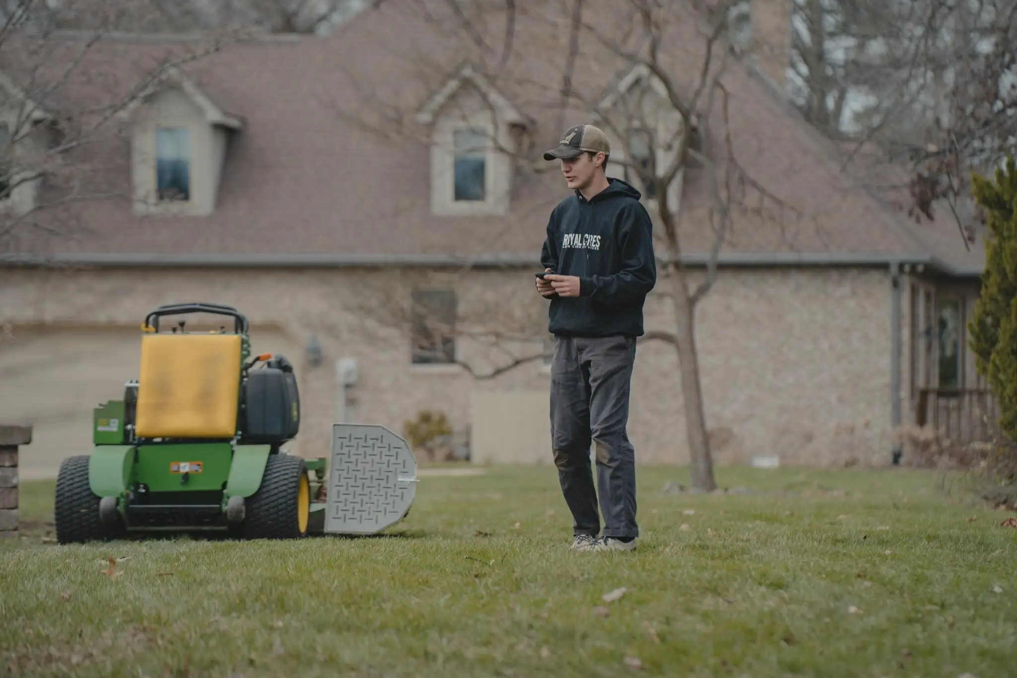 A crew member standing beside a stand-on mower on a front lawn
