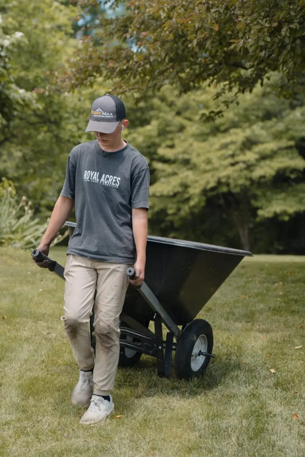 A crew member wheeling a wheelbarrow across a lawn