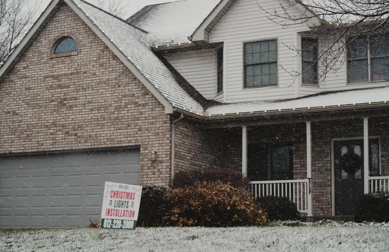 A brick house with a Christmas lights installation sign in the frosted yard