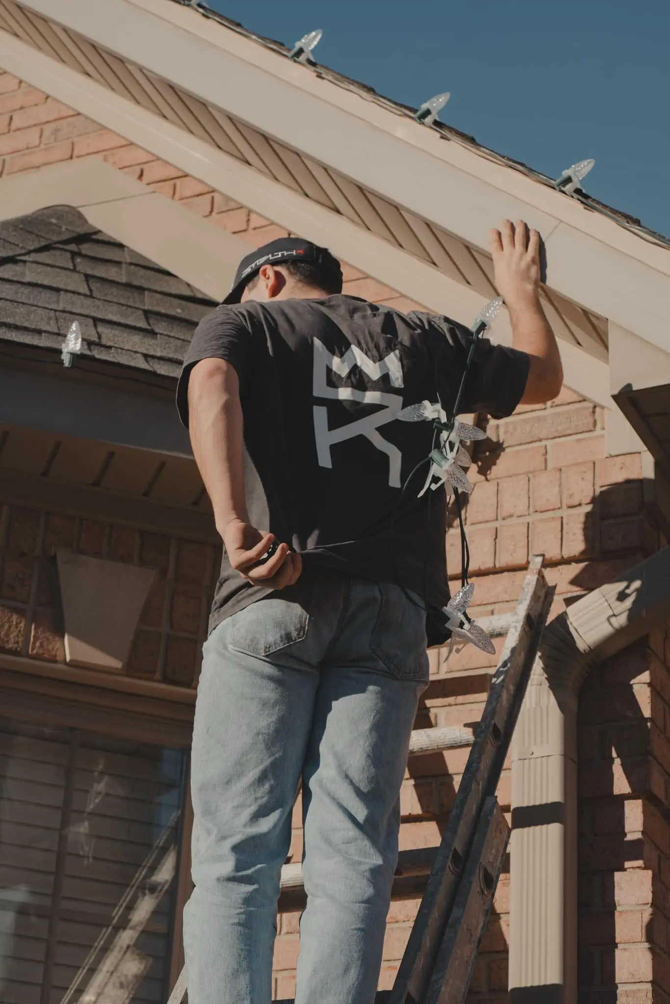 A crew member on a ladder fixing lights along a gable