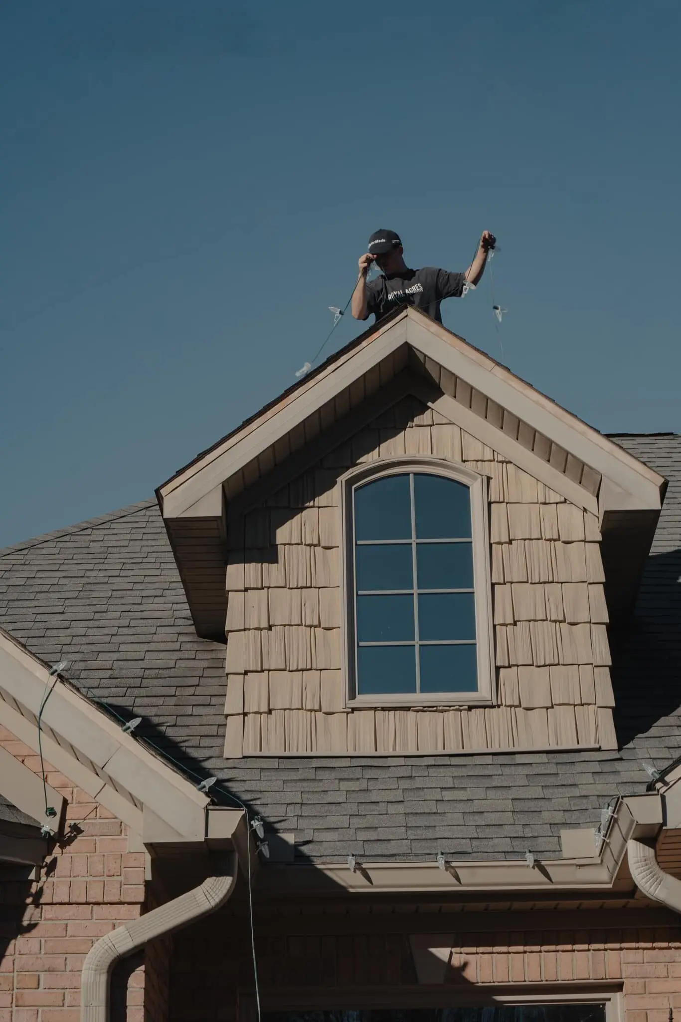 A crew member at the peak of a roof, hanging holiday lights