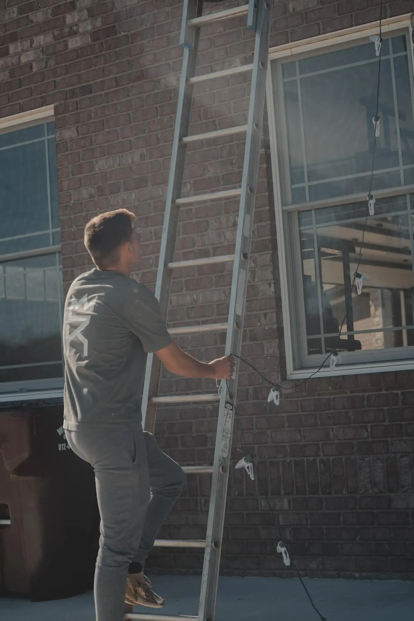 A crew member climbing a ladder against a brick house