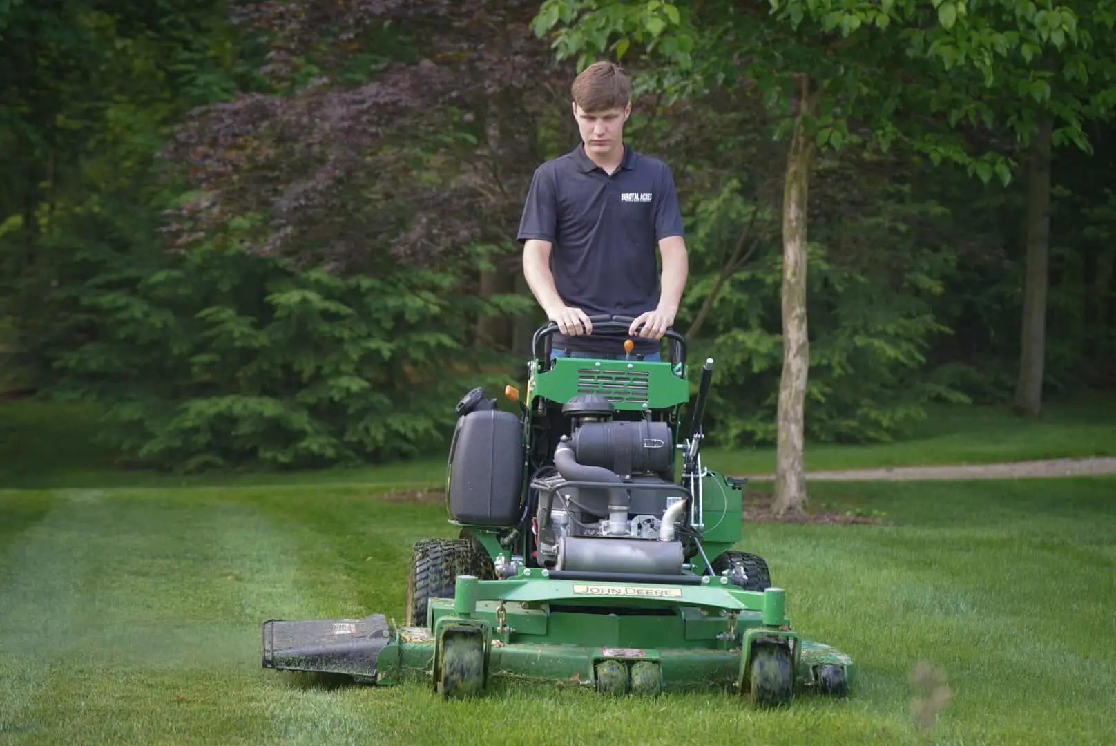A crew member mowing a summer lawn on a stand-on mower