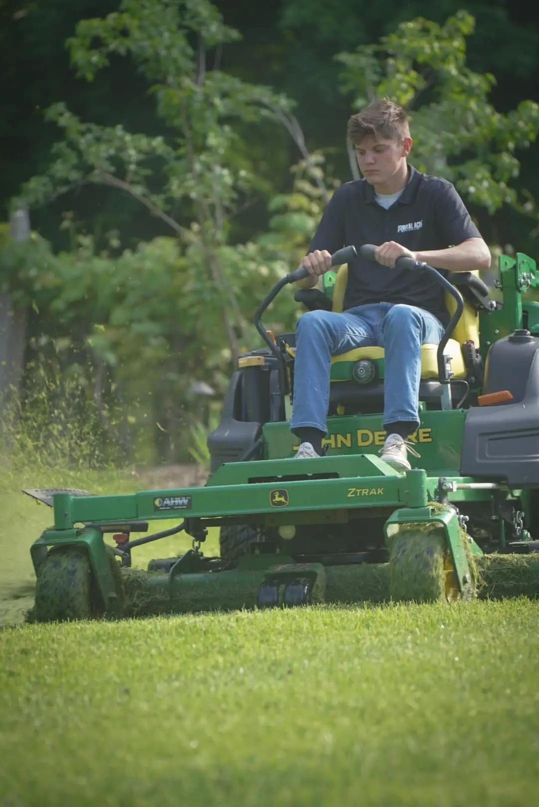 A crew member cutting long grass on a zero-turn mower