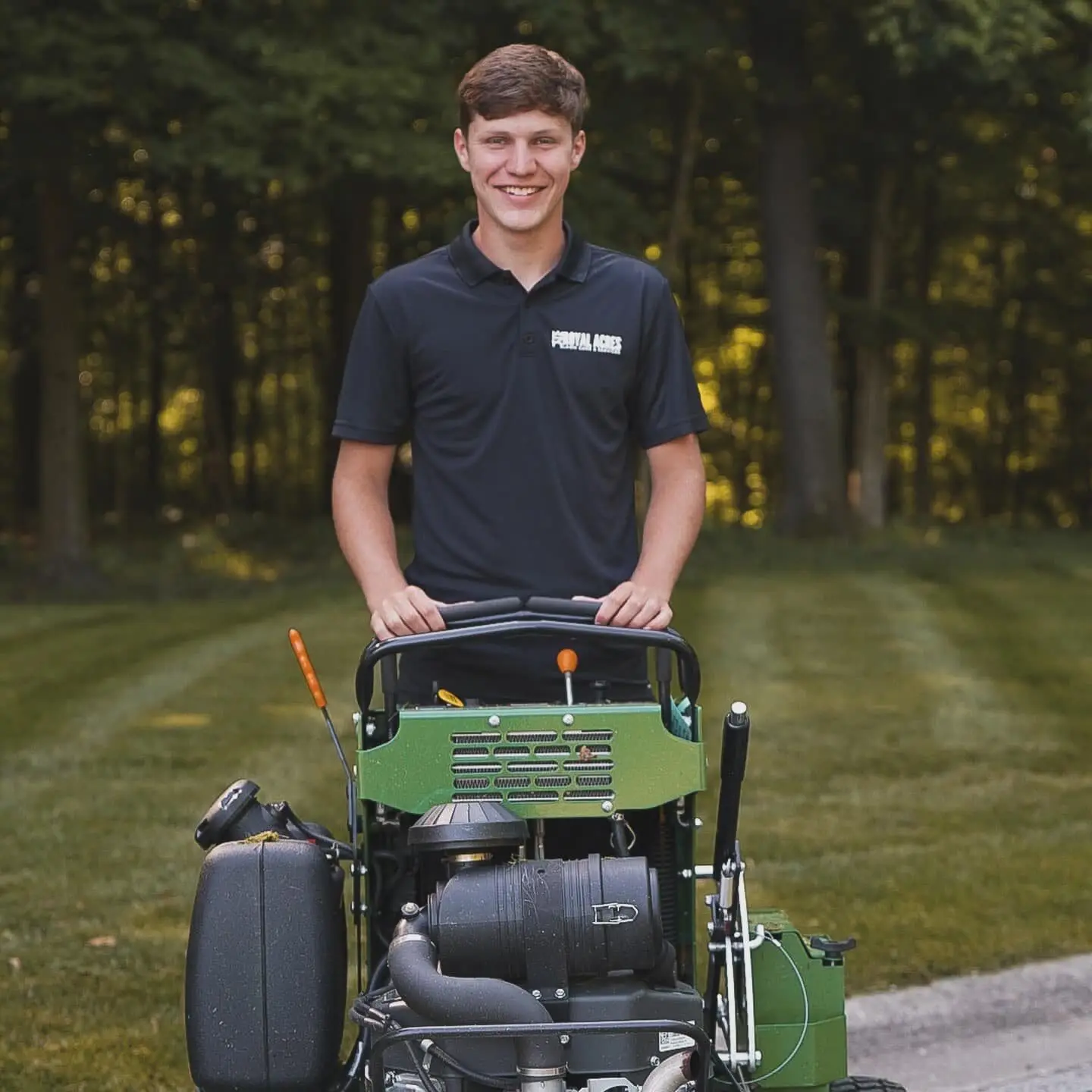 A smiling crew member behind a stand-on mower on a striped lawn