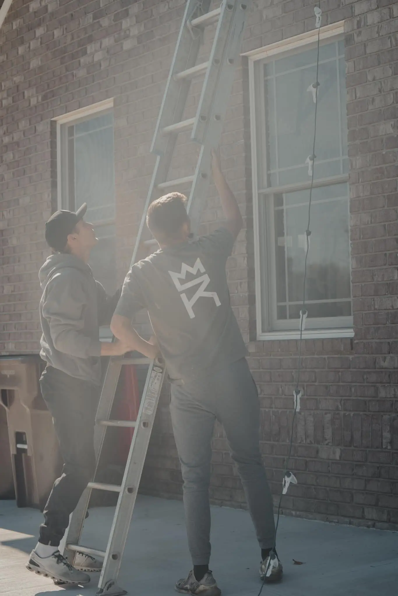 Two of the crew at a ladder against a brick house